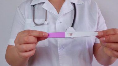Doktor, beyaz arka planda pozitif hamilelik testi gösteriyor.