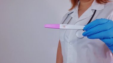 Doktor, beyaz arka planda pozitif hamilelik testi gösteriyor.