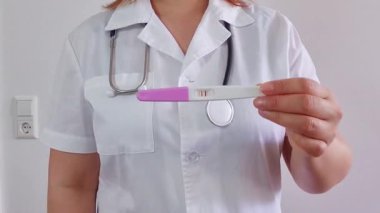 Doktor, beyaz arka planda pozitif hamilelik testi gösteriyor.