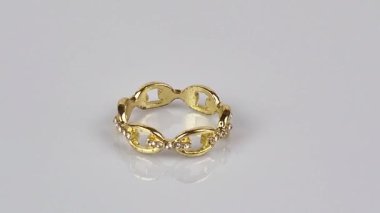 Beyaz arkaplanda dönen taşlı altın yüzük.