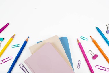 Temiz beyaz bir zemin üzerinde not defterleri, kalemler ve ataçlar içeren renkli bir sayfa..