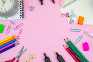 İşaretler, makas ve klipsler gibi renkli çalışma malzemeleri pembe bir arkaplan üzerine ayarlanır