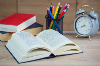 Masanın üzerinde seçici odak ve yüzeysel alan derinliğinde Açık Kitabı okumak için eski bir çalar saat var. Yüksek kalite fotoğraf