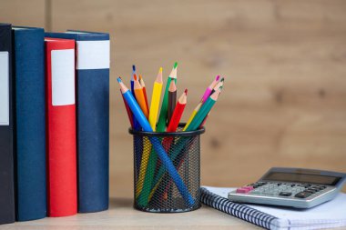 Bir tutacakta renkli kalemler, kitapların yanında ve kolay erişim için hesap makinesi.