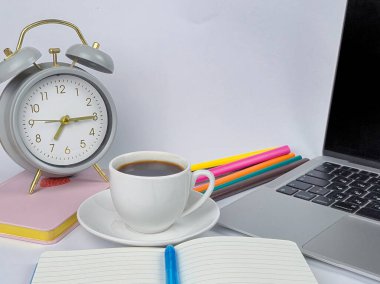 Bir kahve fincanı, bir saat ve bir dizüstü bilgisayarın yer aldığı rahat ve davetkar bir çalışma alanı, odaklanmış çalışma anları için mükemmel.