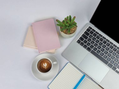Bir dizüstü bilgisayar, bir fincan kahve, defterler ve küçük bir bitkinin sergilendiği çağdaş ve modern bir çalışma ortamı.