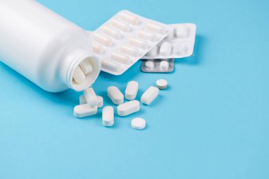 Beyaz bir şişenin etrafında çeşitli su toplayan paketlerinin yanında dökülen ilaçların yakın plan görüntüsü.