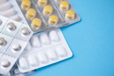 Parlak mavi bir arka planda sergilenen çeşitli ilaç paketlerinin canlı ve renkli bir çeşidi