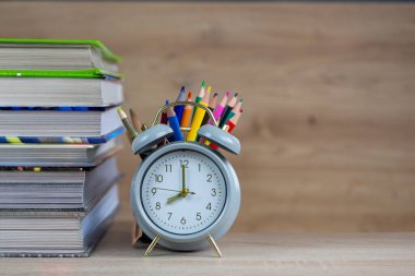 Çekici bir masa düzeneği renkli bir çalar saat ve parlak kalemlerin yanında bir yığın kitap içerir.