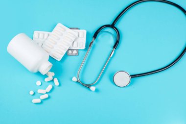 Konteynır, dağınık haplar ve steteskop mavi arka planda izole edilmiş. Yüksek kalite fotoğraf