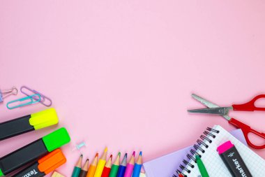 Değişik okul malzemelerinin canlı ve renkli bir koleksiyonu yaratıcı bir şekilde hoş pembe bir arka plana yerleştirilmiş.