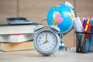 Alarmlı saati, küresi, kitapları ve eğitim ve üretkenlik için gerekli kırtasiyesi olan samimi bir çalışma sahnesi.