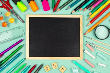 Nane yeşili arka planda boş bir karatahtanın etrafına yerleştirilmiş canlı bir ofis malzemesi koleksiyonu..