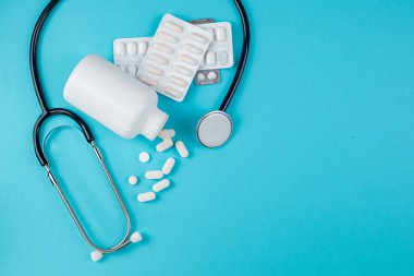 Konteynır, dağınık haplar ve steteskop mavi arka planda izole edilmiş. Yüksek kalite fotoğraf