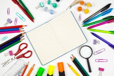 Renkli kırtasiye malzemeleri temiz beyaz bir arkaplan üzerinde boş bir defter etrafında güzelce düzenlenir