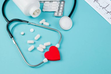 Kalp sağlığı ilaçlarının düzenlenmesi, steteskop ve turkuaz arka planda ECG şeması..