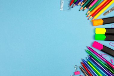 Bir dizi canlı ve renkli kırtasiye malzemesi mavi arka planda sanatsal bir şekilde düzenlenmiş.