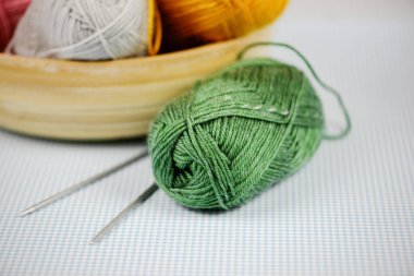 Renkli bir sepetin içine yerleştirilmiş, dingin, yeşil iplik ve örgü iğneleri sergilenen güzel bir resim.