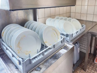 Mutfak odasındaki restoranda otomatik bulaşık makinesi tarafından temizlenmesi için sepete yerleştirilmiş bir sürü tabak veya beyaz tabak var. Yüksek kalite fotoğraf