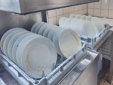 Mutfak odasındaki restoranda otomatik bulaşık makinesi tarafından temizlenmesi için sepete yerleştirilmiş bir sürü tabak veya beyaz tabak var. Yüksek kalite fotoğraf