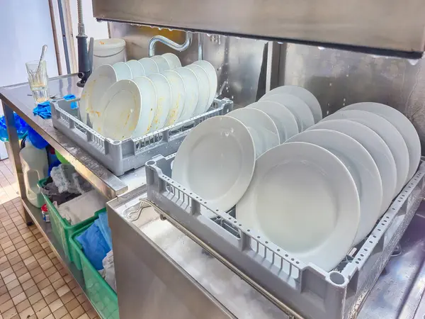 Mutfak odasındaki restoranda otomatik bulaşık makinesi tarafından temizlenmesi için sepete yerleştirilmiş bir sürü tabak veya beyaz tabak var. Yüksek kalite fotoğraf