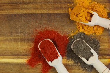 Paprika, zerdeçal ve karabiber içeren canlı baharat koleksiyonu, ahşap üzerine güzelce yerleştirilmiş.