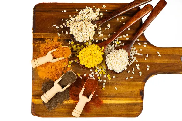 Kırsal bir ahşap kesme tahtasına ustalıkla yerleştirilmiş çeşitli tahıl ve baharatların canlı ve renkli bir görüntüsü.