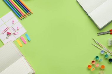 Çeşitli yaratıcı projeler için yeşil bir yüzeye yerleştirilmiş renkli sanat materyalleri ve kırtasiye öğeleri