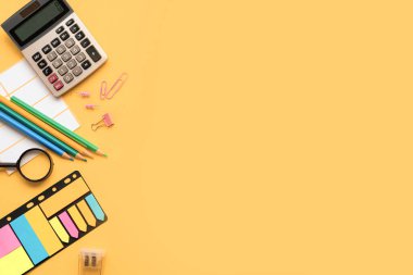 Hesap makinesi gibi hareketli ofis malzemeleri, renkli kalemler ve parlak sarı arka planda ataçlar.