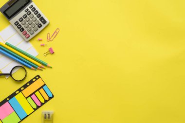 Parlak renkli ve enerjik ofis malzemeleri parlak sarı bir yüzey üzerinde yaratıcı bir şekilde düzenlenmiştir.