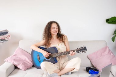 Neşeli bir kadın evinde akustik gitarını çalarak kanepesinde dinlenirken müziğin keyfini çıkarıyor.