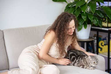 Bir kadın, şık ve rahat bir yaşam alanına yerleşmiş sevgili kedisiyle güzel vakit geçiriyor.