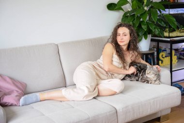 Bir kadın evinde huzurlu bir anın tadını çıkarıyor, rahat bir kanepede dinlenirken sevgili kedisiyle sarılıyor.