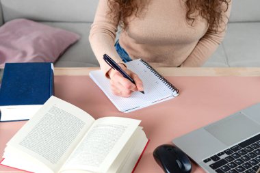 Çeşitli kitapların arasında çalışırken özenle not alan ve dizüstü bilgisayar kullanan bir birey.