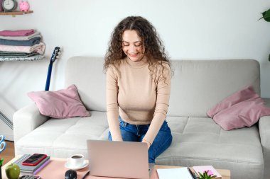Genç bir kadın dizüstü bilgisayarı üzerinde özenle çalışıyor. Yaratıcılığına ve odaklanmasına ilham veren sıcak ve rahat bir yerde.