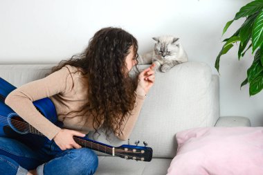 Bir kadın, evinde gitar çalarken sevgili kedisiyle sevgi dolu bir şekilde bağ kurarken sıcak bir an başlıyor.