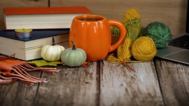 Turuncu bir kupa, canlı bir iplik, mini balkabakları ve ilginç kitaplar içeren samimi ve ılık bir sonbahar ortamı.