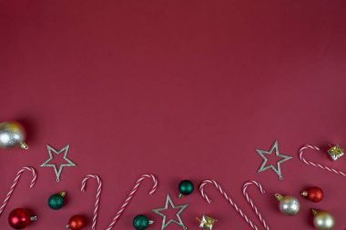 Neşeli bayram ruhunu canlı Noel süsleri ve zengin kırmızı bir zemin üzerinde renkli şekerlerle kutlayın.