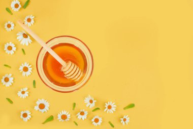 Canlı sarı bir zemin üzerinde papatyalarla çevrili bir bal kasesi, sağlık ve sağlık teması için mükemmel..