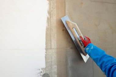 Builder plastering the wall with a spatula, fiberglass mesh, after insulating the house