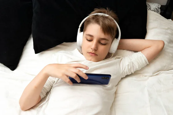 Bored teenager boy with mobile phone watching videos or websites laying on the bad at home
