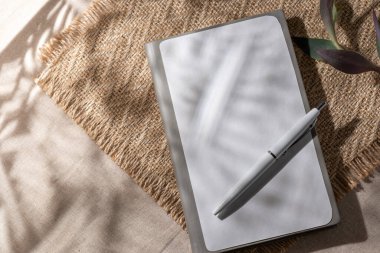 Blank paper notebook sheet with mockup copy space and a floral sunlight shadows on beige background. Flat lay, top view minimalist business brand template