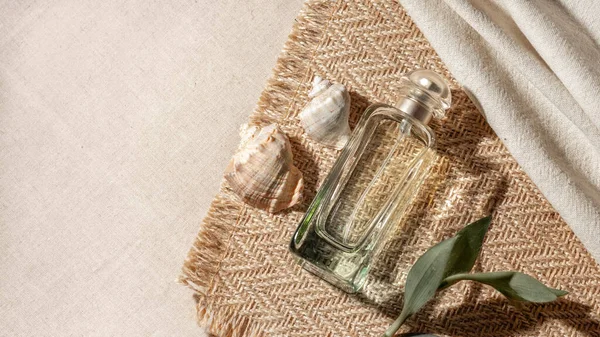 Beauty natural aesthetic summer background with perfume bottle and sea shells on beige textile background.