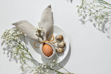 Minimalist Paskalya estetik masası, tabakta tavşan kulağı peçetesiyle süslenmiş yumurta. Fotokopi alanı olan tarafsız çiçek arkaplanı. Bayram bahar şablonu veya pankart tasarımı