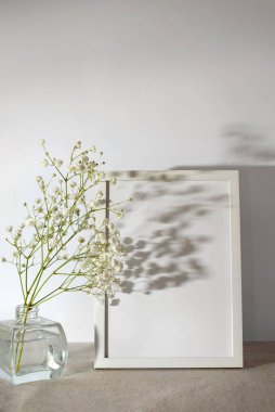 Boş kopya alanına sahip boş çerçeve, beyaz arka planda çiçekler ve güneş ışığı gölgeleri, minimalist yaşam tarzı iç mekan şablonu