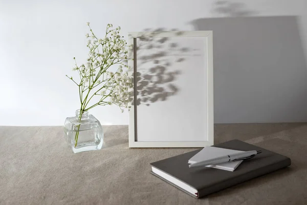 コピースペース付きの空のフレーム 花の花束 白い背景に日光の影を持つテーブルの上のノートブック ミニマリストのパステル静物画 ワークスペース — ストック写真