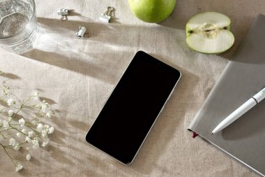 Estetik iş geçmişi, bej bir masa örtüsünün üzerinde cep telefonu ve güneş ışığı gölgeleri olan düz bir yer.