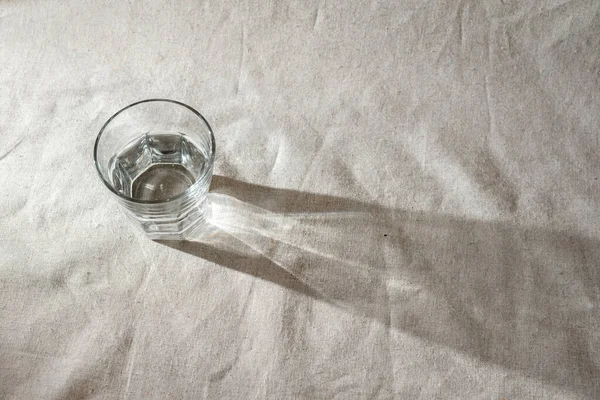 Ένα Ποτήρι Νερό Ένα Μπεζ Λινό Τραπεζομάντηλο Σκιές Ηλιακού Φωτός — Φωτογραφία Αρχείου