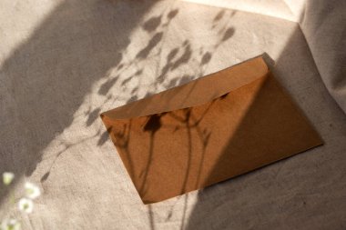 Tarafsız bej bir arka planda el yapımı kahverengi zarf. Sert güneş ışığı gölgeleri, minimalist estetik markalaşma kompozisyonu.