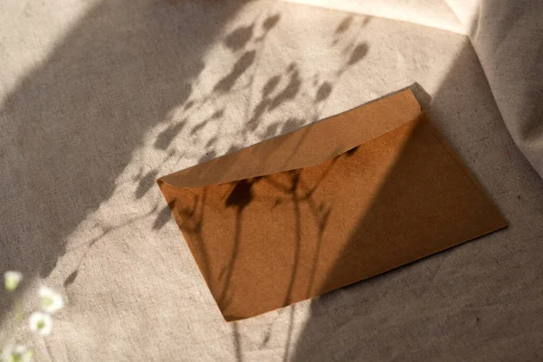中性米色亚麻布背景上手工制成的棕色信封 有刺眼的阳光花纹 极简主义美学品牌构图 — 图库照片